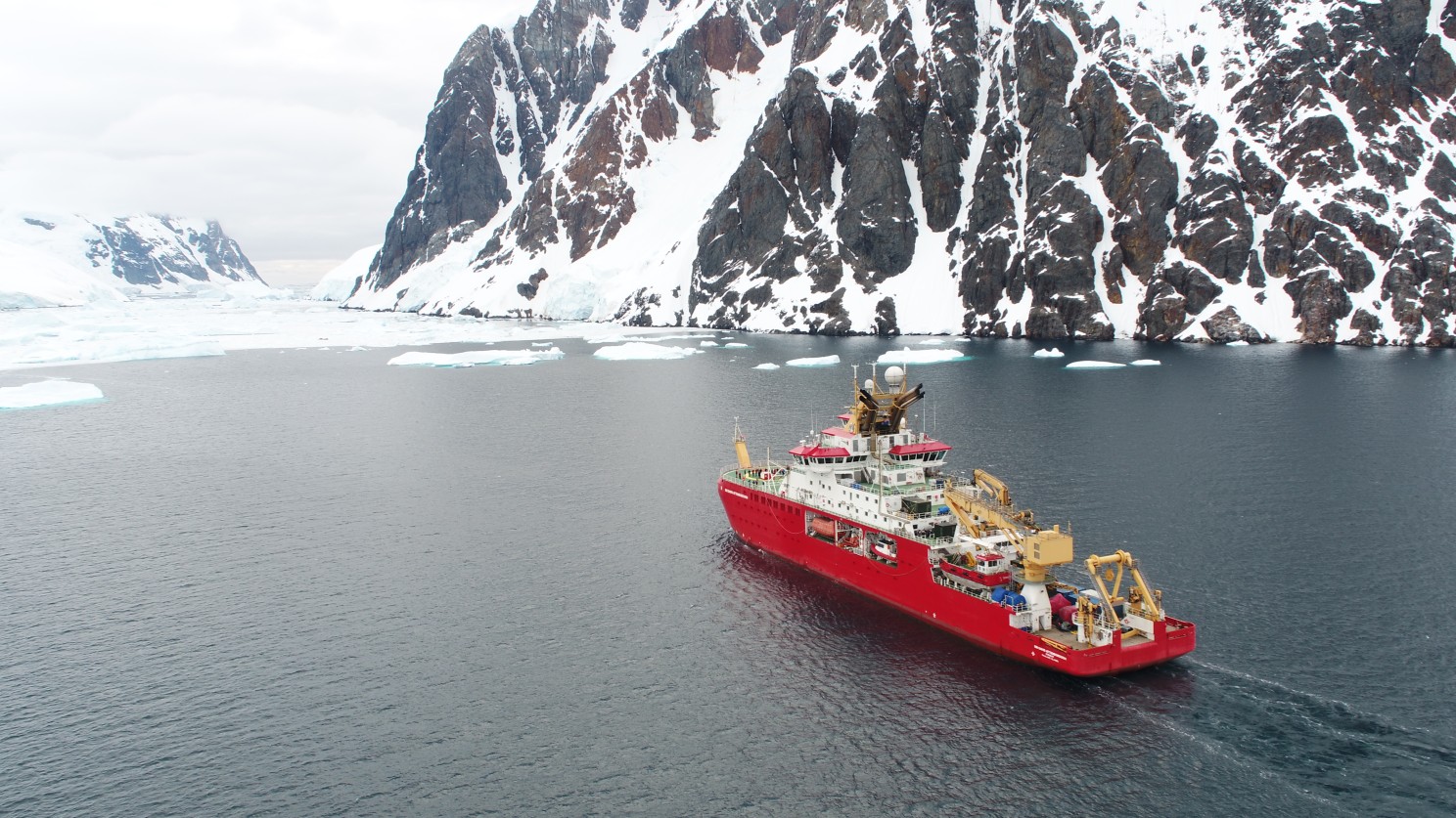 A large red ship sailing in Antarctica with a large rocky mountain on the right