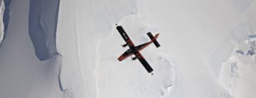 A plane flying through the air above an icy landscape