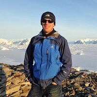 A man standing next to a body of water posing for the camera
