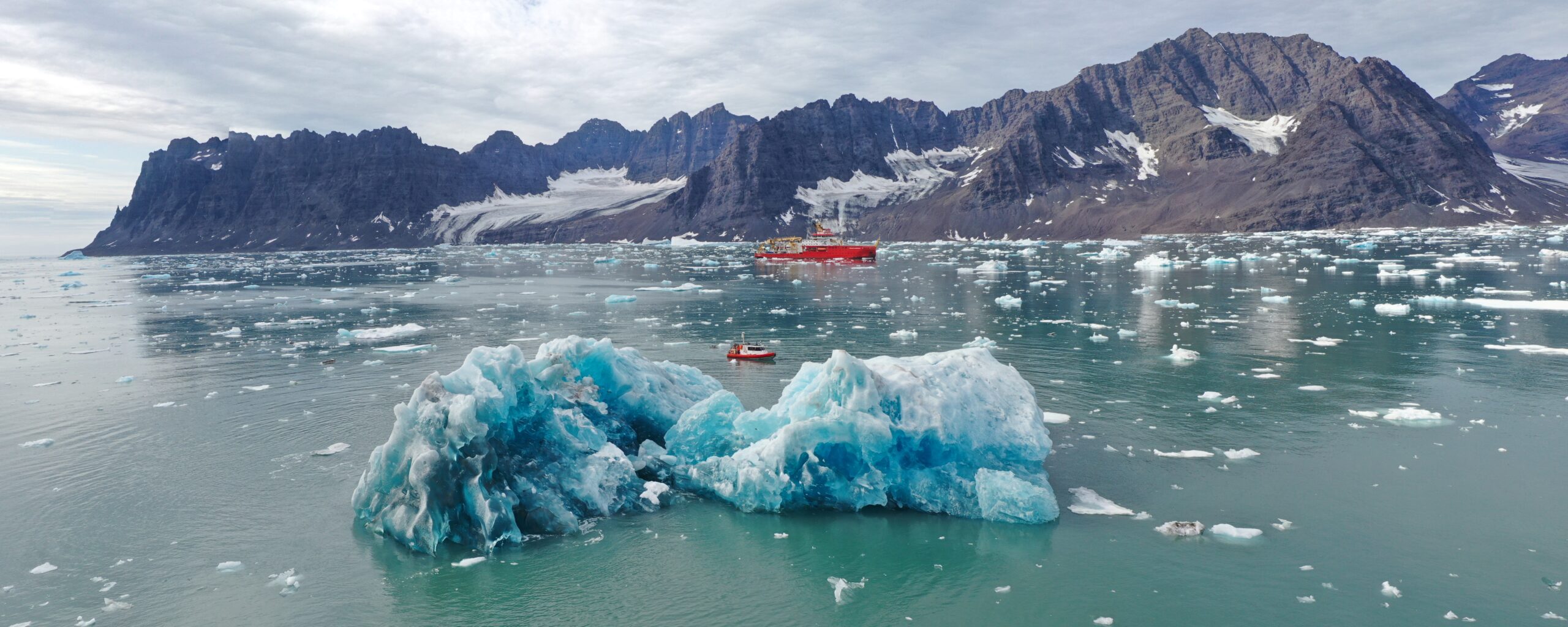 The RRS Sir David Attenborough sailing behind an Iceberg in Greenland