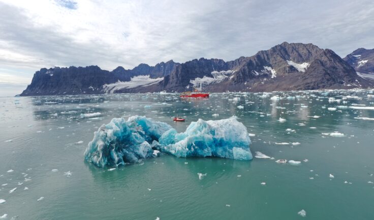 The RRS Sir David Attenborough sailing behind an Iceberg in Greenland