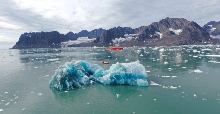The RRS Sir David Attenborough sailing behind an Iceberg in Greenland