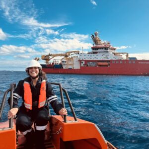 A smiling female on a small boat with the RRS Sir David Attenborough in the background