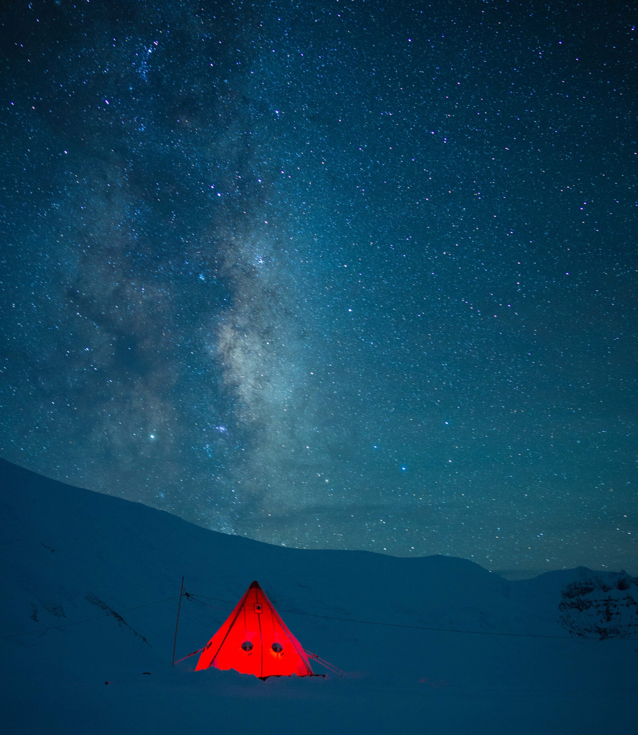 Bright red pyramid tent under the Milky Way during a winter trip.