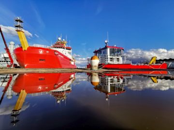 A large red ship next to a smaller red workboat
