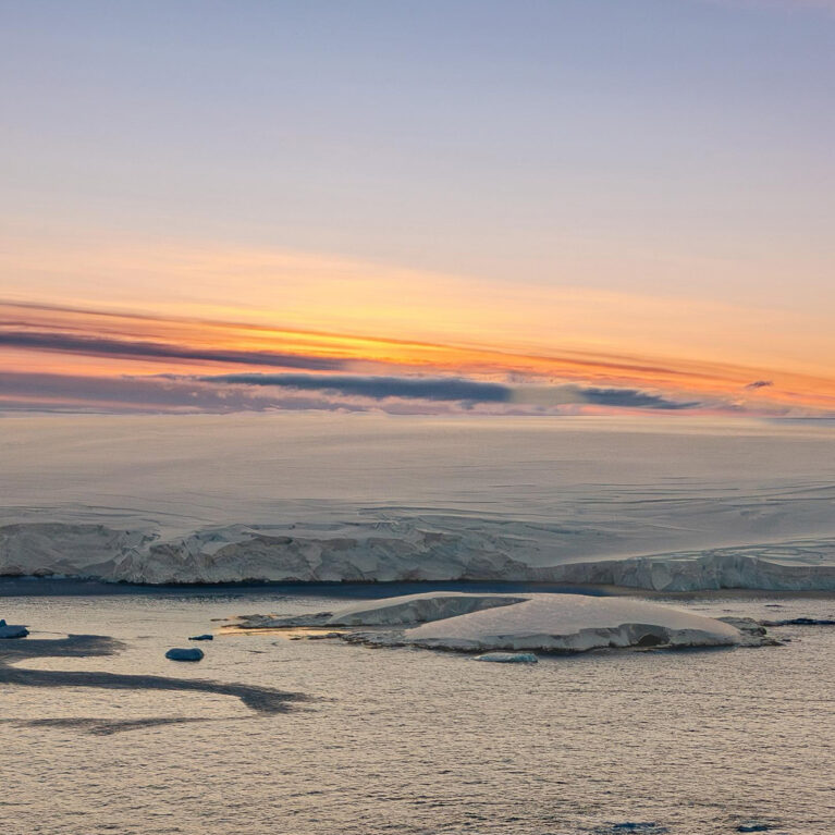 An Antarctic sunset. The ice shelf meets the sea with mountains in the background