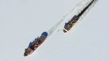 Two large boats saliing through sea ice