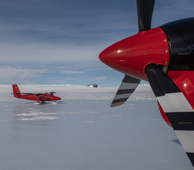 Two twin otter propeller planes that have landed on blue ice.