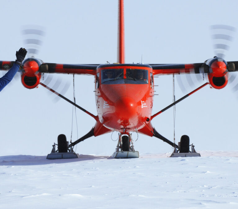 A red twin otter plane landing on skis