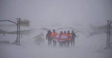 A group of people walking across snow covered ground, holding a flag